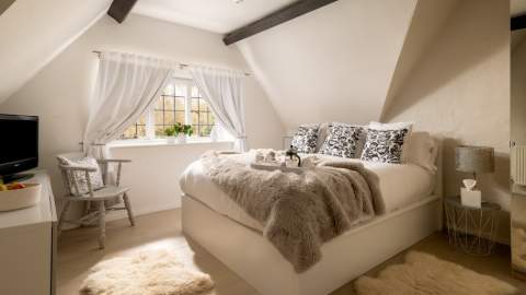 Bedroom in cottage with furry bedspread and wooden beams