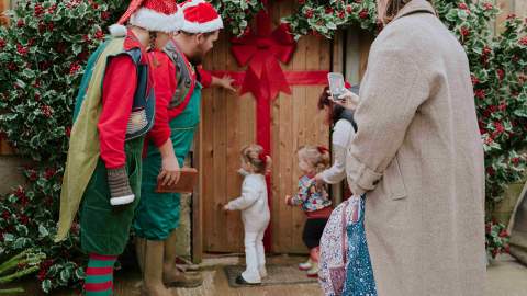 Two young children tentatively entering Santa's grotto with two 'elves'