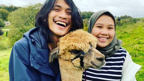 Two people smiling and posing with an alpaca