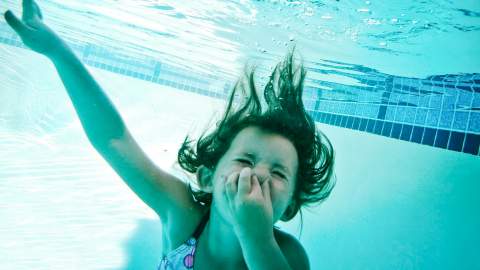 Jente som holder seg for nesen under vann i et svømmebasseng. Foto.