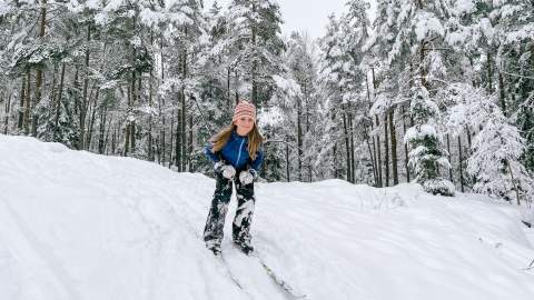 Barn som står på ski ned en bakke i skogen. Foto.