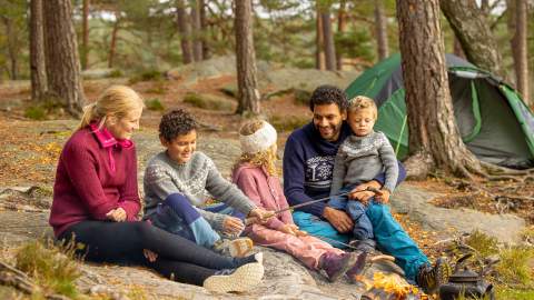 Familie på tur i skogen hvor de griller pølser.