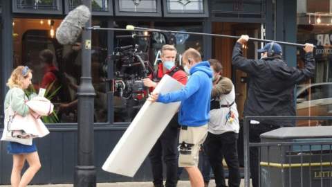 Filming of tv show Hullrasiers on Newland Avenue in Hull. An actress stands outside a shop whilst a camera crew stand before her with a board and a boom microphone.