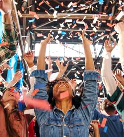 People with their arms up, cheering and confetti falls on them