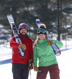 A man and a woman in ski gear and carrying skis while posing for a photo