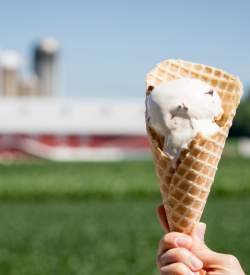 A hand holding up a cone of ice cream in front of a barn
