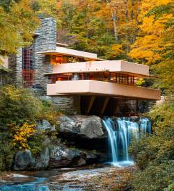 Iconic architectural building Fallingwater sits atop a waterfall with fall foliage surrounding.