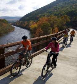 Family bikes across a bridge with mountains and a river in the background