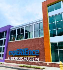 Exterior of a two-story museum with a large sign in front that reads Experience Childrens Museum