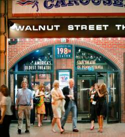 People exiting a theater entrance. A sign above the entrance reads Walnut Street Theatre