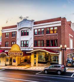 Exterior of an old school theatre on a Main Street with a brightly lit gold sign in the front that reads The Palace.