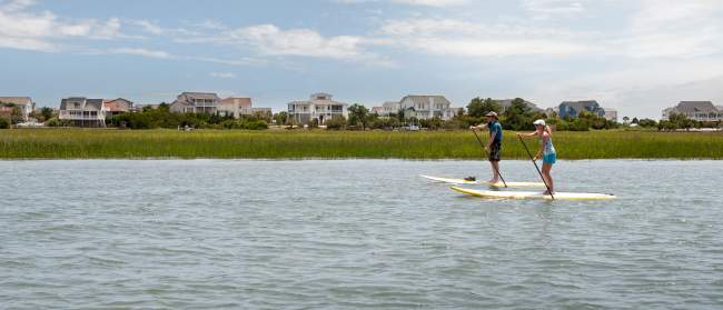 a couple paddleboarding in the marsh