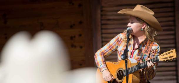 Performer with a guitar wearing a cowboy hat on stage.