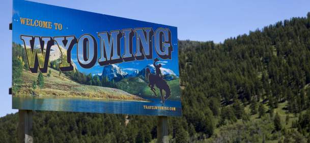 The Welcome to Wyoming road sign set against a forest covered mountain side.
