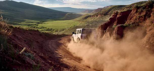 a dusty road with a vehcile driving along it through landscape