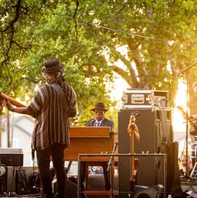 Booker T. Jones (on the piano) and his band members. The image is taken from the back of the stage and there is music equipment and speakers throughout the stage.
