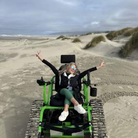 Kirstin with her arms raised in celebration in a track chair on the beach.