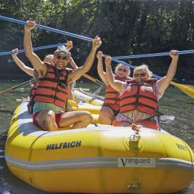 River rafters in a yellow raft hold their paddles triumphantly over their heads.