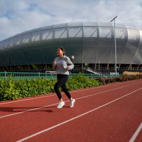 A woman running on a track surface in front of Hayward Field.