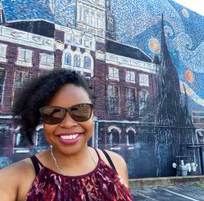 lady smiling in front of a large mural