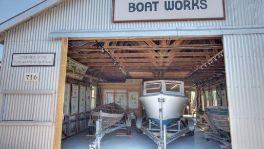 A white boat sits on a trailer inside a building with a sign reading "Farley Boat Works."