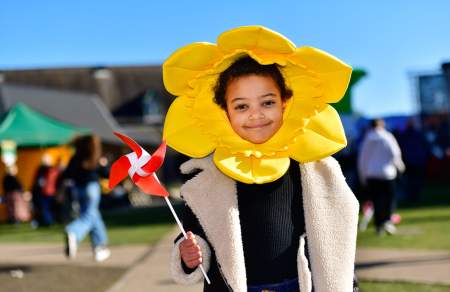 A child wearing a daffodil head dress, holding a windmill.