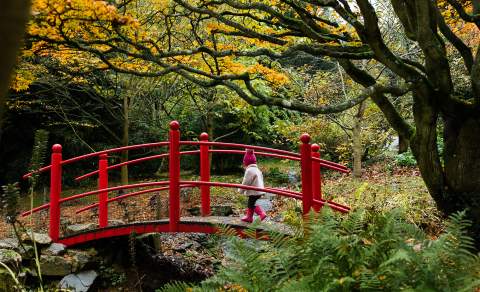 Child in bobble hat and pink coat crossing a bridge at Batsford Arboretum