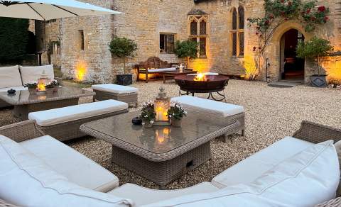 Outdoor sofas and tables sit in a courtyard lit by lanterns and a firepit at Abbots Grange Manor House in the Cotswolds