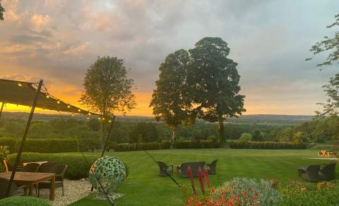 The garden of the Feathered Nest Country Inn with extensive lawn, sculpture and seating with the sun setting across the hills in the distance