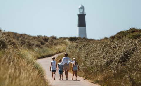 A family walking a winding path towards the iconic black and white Spurn Lighthouse in East Yorkshire