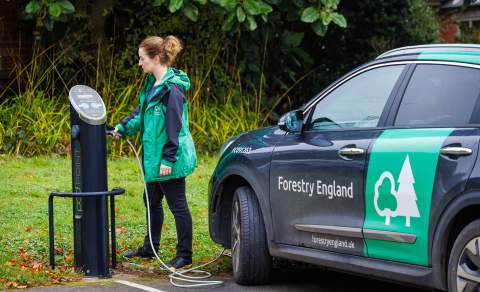 A woman plugs in an electric vehicle for charging at Westonbirt, The National Arboretum