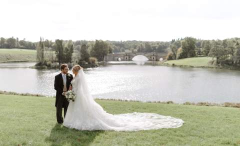 A bride and groom smiling at each other infront of the Great Lake at Blenhaim Palace