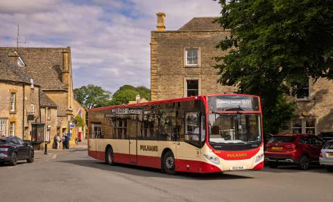 The single-decker Pulham's 801 bus driving along a street with honey-coloured buildings in Stow on the Wold