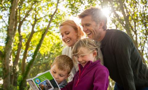 A smiling family look at a treasure trail leaflet in a woodland