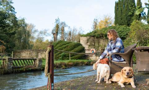 Woman with two dogs sat on a bench by the river at Minster Mill