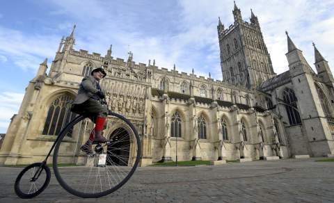Man on a penny farthing bicycle in front of Gloucester Cathedral