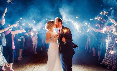 A newlywed couple kiss outside in the dark holding sparklers, while their guests hold sparklers around them at Ellenborough Park