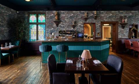 Patterned wallpaper, a stained glass window, a dark blue ceiling and green tiled bar create a truly unique dining room at Abbey Row, The Old Bell Hotel in the Cotswolds