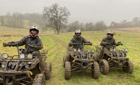 Three men ride mud splattered quad bikes in a field