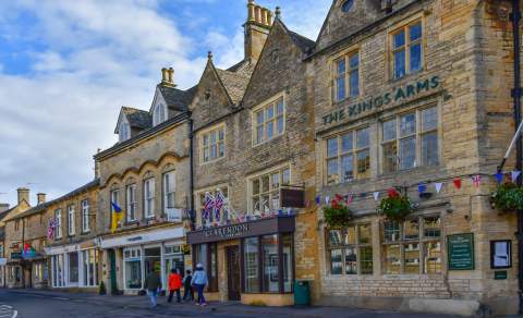 A family walking past shops of honey-coloured Cotswold stone in Stow on the Wold, in the Cotswolds