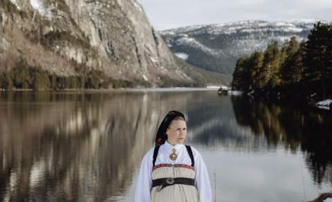 Young lady wearing national costume standing next to the river and steep mountains in Setesdal. Photo