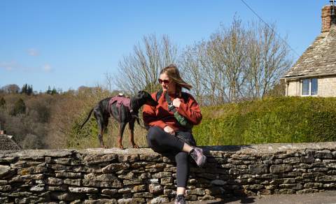 Lottie Gross with her dog sat on a Cotswold stone wall