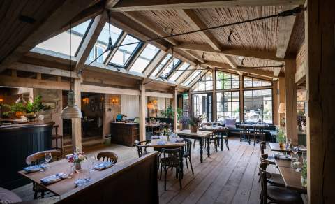 A large wooden conservatory with tables dressed for dinner with fresh flowers at Royal Oak Ramsden in the Cotswolds