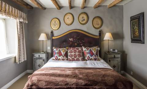 A room with a beamed ceiling and double bed with decorative cushions