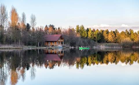 A cabin looks over a lake on a bright winter day at Log House Holidays
