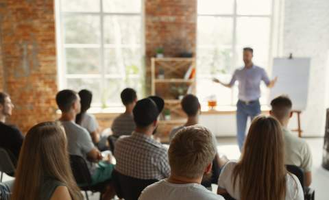 A person talks to a group of people seated in rows at a business event
