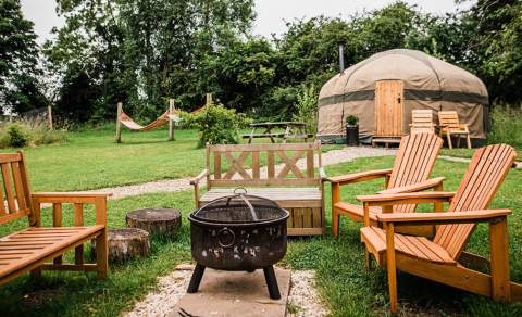 Yurt in background with chairs around firepit in foreground