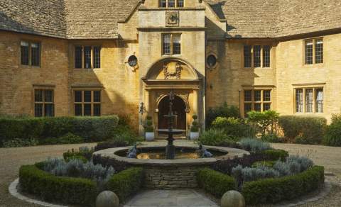 A circular fountain surrounded by topiary creates a stunning centrepiece in front of the entrance to the impressive honey-coloured stone Foxhill Manor