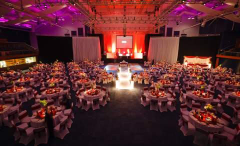 A large room with stage and large screen, and tables dressed for a gala dinner at Cheltenham Racecourse