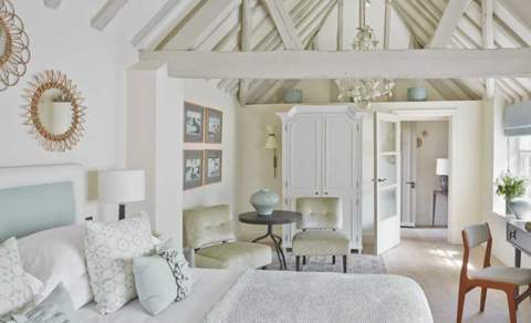 A light and airy bedroom with white washed rafters over a large bed with cosy blanket and pillows